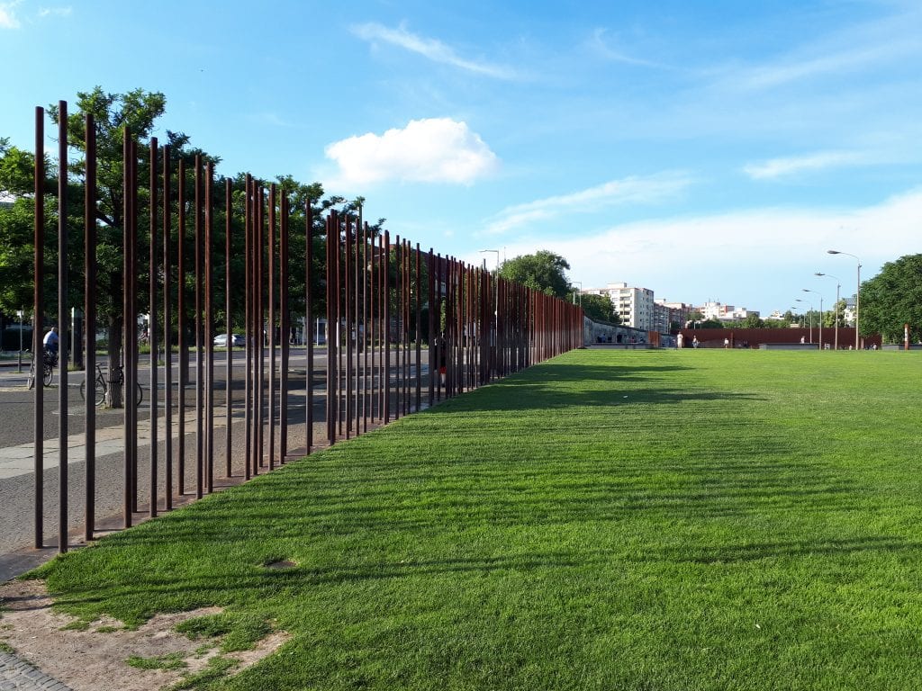 Památník Berlínské zdi. Tyče naznačují kudy zeď vedla, v pozadí jsou dochované pozůstatky.